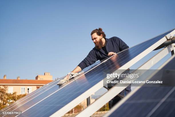 bearded worker using cloth to clean solar panels - selbständige erwerbstätigkeit stock-fotos und bilder