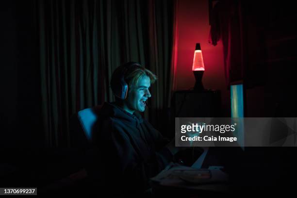 smiling teenage boy playing video game at computer in dark bedroom - slaapkamer zijaanzicht stockfoto's en -beelden