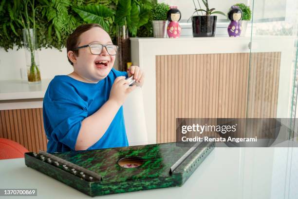 boy with down syndrome learning music. playing harp and harmonica at home. - jonglieren stockfoto's en -beelden