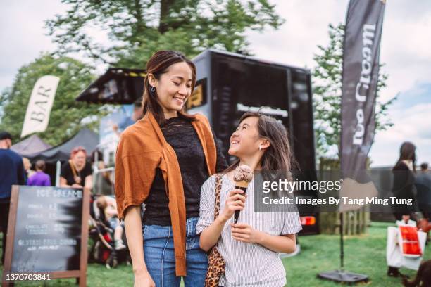 lovely girl enjoying ice cream with her young pretty mom in front of a food truck at food festival - mother and child snacking stockfoto's en -beelden
