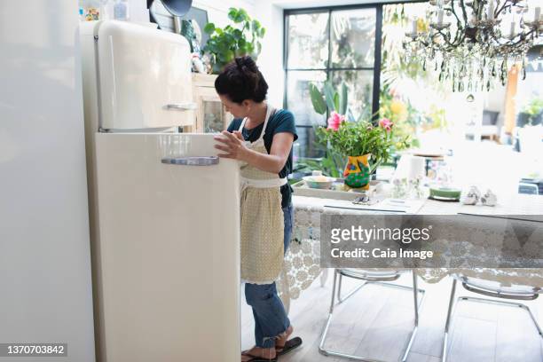 woman in apron standing at open refrigerator in kitchen - open fridge ストックフォトと画像