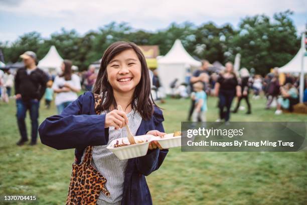 lovely girl enjoying take away food at a food festival - furgón de comida fotografías e imágenes de stock