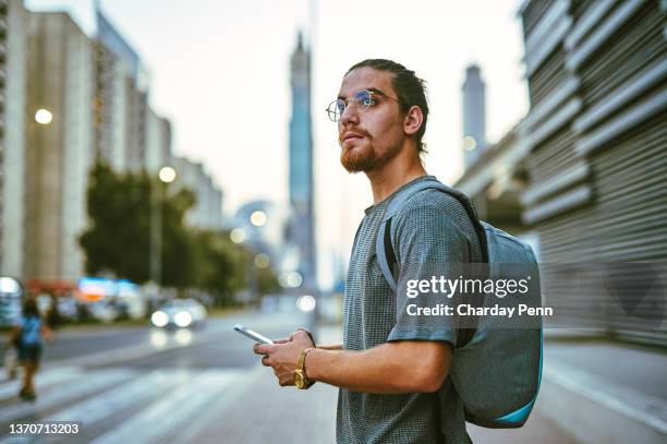 shot of a handsome young man standing alone in the city and looking contemplative while using his cellphone - searching on phone stockfoto's en -beelden