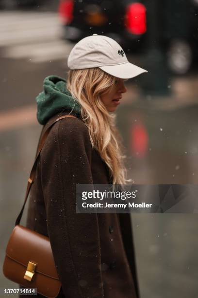Guest wears a white latte cap with black embroidered pattern, a dark green hoodie sweater, a dark brown long wool coat, dark green and khaki with...