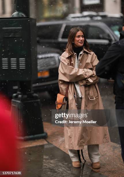 Amanda Alagem wears a tan trench coat over a white outfit and tan suede boots at the Ulla Johnson show at New York Public Library on February 13,...