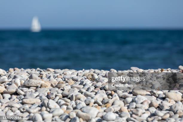 pebbles on the coastline with sailboat in background - beach stone stock pictures, royalty-free photos & images