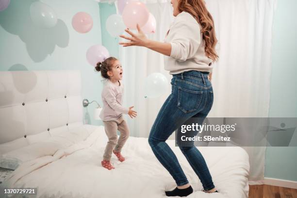 little girl plays with her mother throwing balloons and jumping on the bed - hovering mom stock pictures, royalty-free photos & images