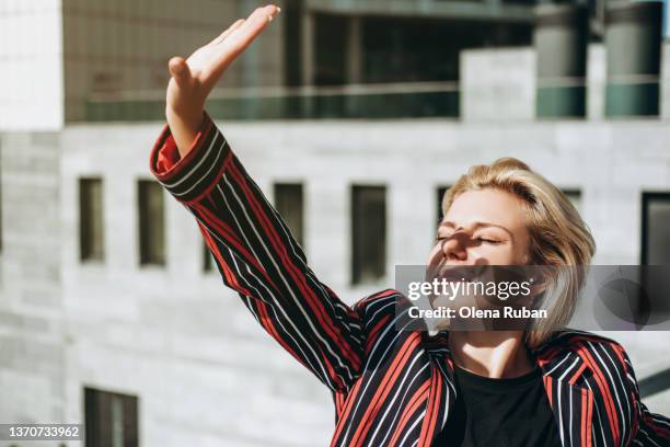 young woman holding hand up to protect from the sun. - cligner des yeux photos et images de collection