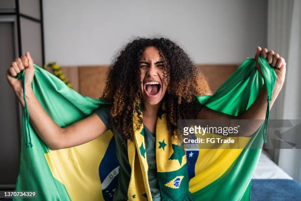 aufgeregte junge frau feiert mit brasilianischer flagge - female fans brazil stock-fotos und bilder