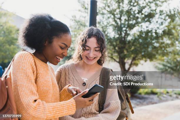 teen girl shows friend something on her smart phone - best friends teenagers imagens e fotografias de stock