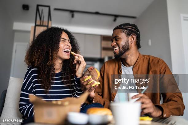 glückliches junges paar, das zu hause fast food isst - snacks stock-fotos und bilder