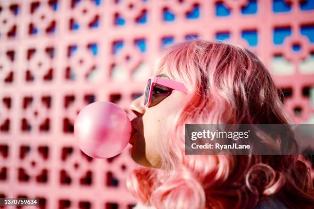 femme aux cheveux roses soufflant une bulle de gomme - mâchonné photos et images de collection