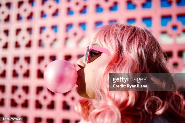 pink haired woman blowing gum bubble - kauwen stockfoto's en -beelden