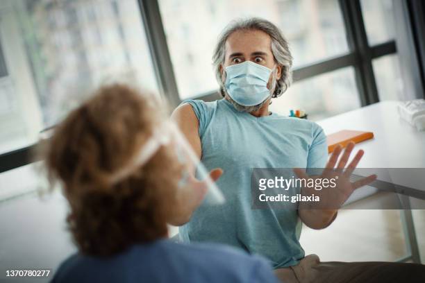 terrified mid adult man receiving covid-19 vaccine. - receiving treatment concerned stock pictures, royalty-free photos & images
