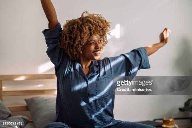 portrait of a happy woman waking up and stretching in bed - waking up stock pictures, royalty-free photos & images