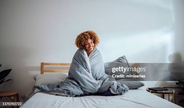 bella donna a letto rannicchiata sotto le coperte che si gode una tazza di tè - avvolto foto e immagini stock