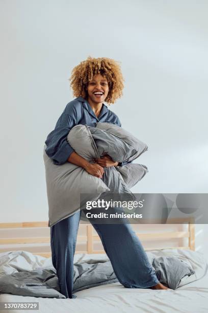 fröhliche frau, die morgens mit kissen auf dem bett spielt - silk pillow stock-fotos und bilder