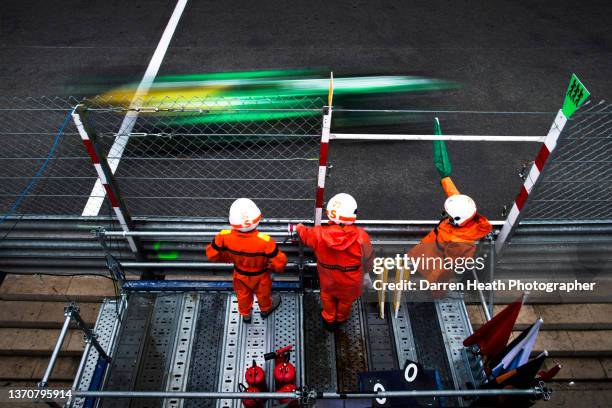 French Caterham British Formula One team racing driver Charles Pic driving his CT03 racing car at speed past three circuit safety marshals wearing...