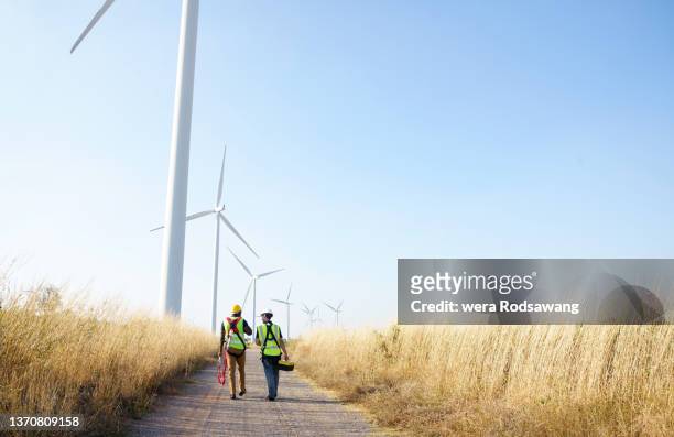 wide perspective of wind turbine engineers walking with coworker in wind farms - power imagens e fotografias de stock