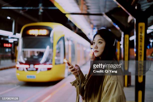 confident asian woman using smartphone at light rail platform - shanghai calling stock pictures, royalty-free photos & images