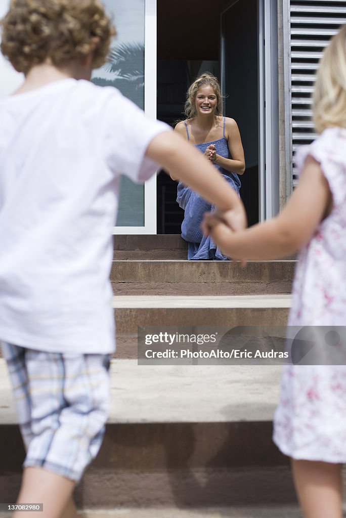 Young siblings holding hands, running toward mother