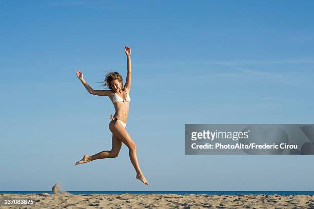 woman jumping in midair at the beach - junge frau strand sand springen stock-fotos und bilder