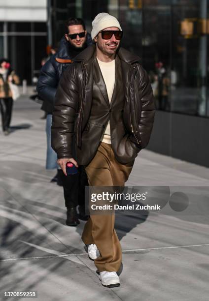 Alex Badia is seen wearing a brown faux leather jacket, cream sweater, cream beanie and tan pants outside the Peter Do show during New York Fashion...