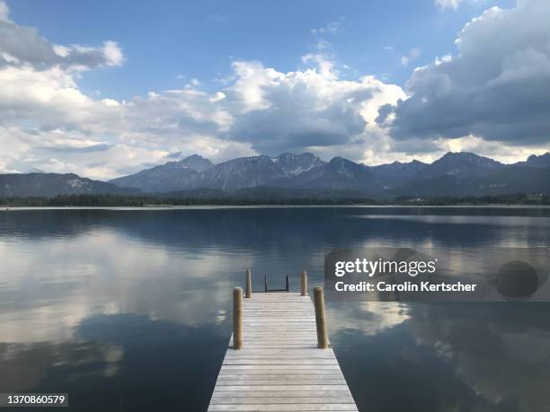 summer day at lake hopfensee with wooden pier, reflection and mountain peaks in the background | germany - boardwalk stock-fotos und bilder