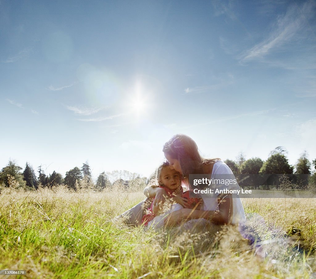 Mother kissing daughter's forehead in rural field