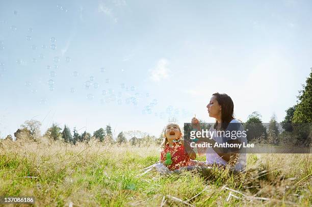 mother and daughter blowing bubbles in sunny rural field - child blowing bubbles stockfoto's en -beelden