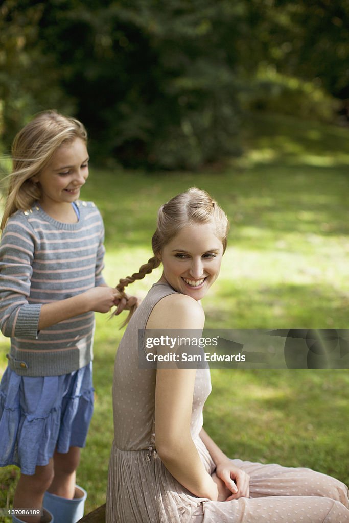 Girl braiding sister's blonde hair in park