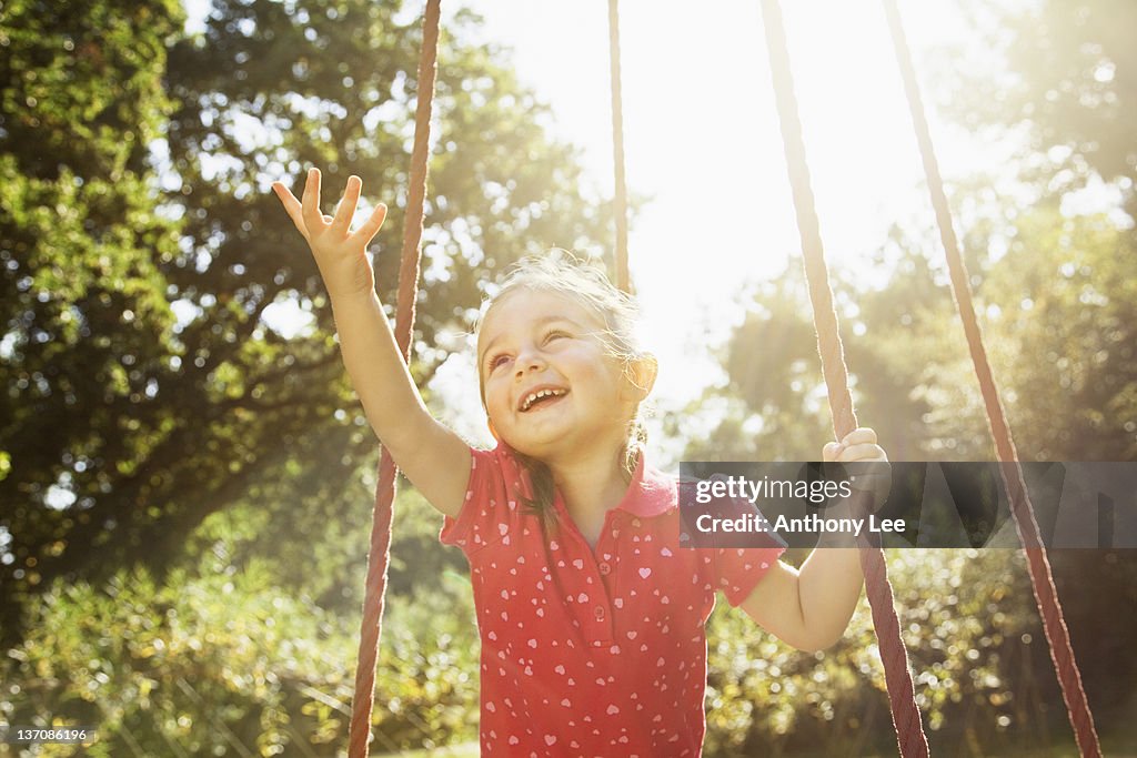 Smiling girl with arm outstretched on swing in sunny park