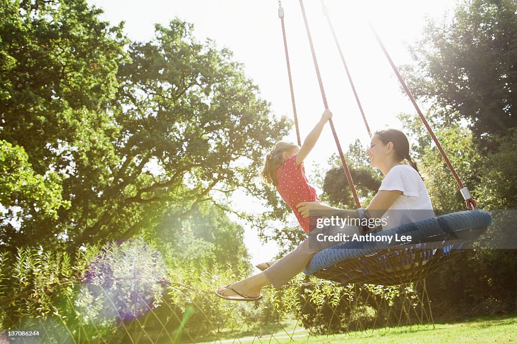 Mother and daughter on swing in sunny park
