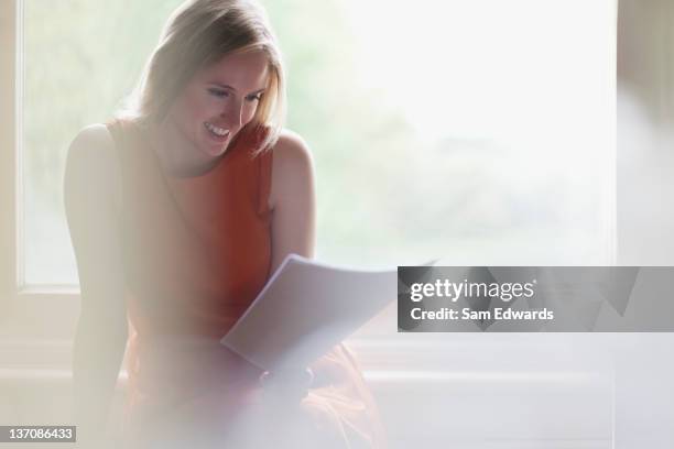 souriant femme lisant une lettre en face de la fenêtre - flouté photos et images de collection