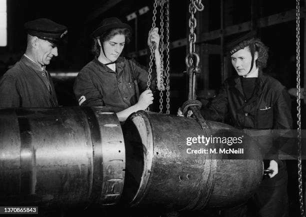 Two Wren Torpedoman of the Women's Royal Naval Service hoist a new explosive nose section using a block and tackle chain to a 21-inch submarine...