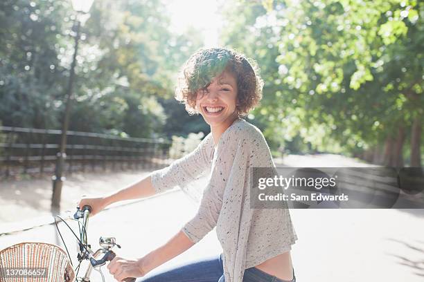 portrait of smiling woman riding bicycle in sunny park - women on bike stockfoto's en -beelden