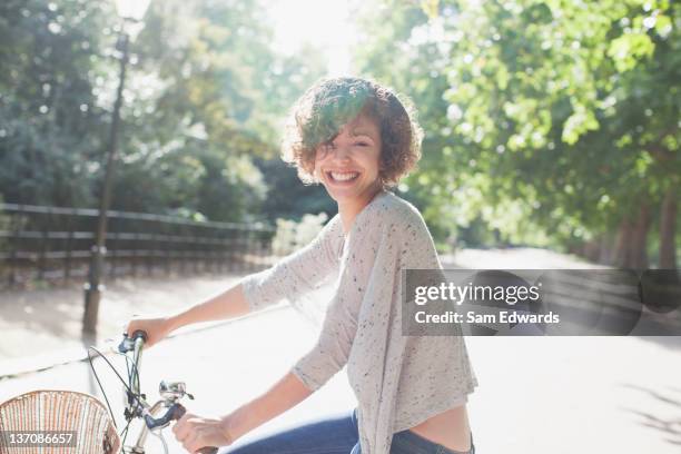 portrait of smiling woman riding bicycle in sunny park - women cycling stock pictures, royalty-free photos & images