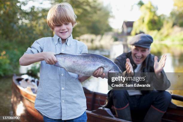 grandson holding fish with grandfather clapping in background - congratulating child stock pictures, royalty-free photos & images