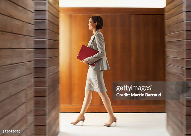 geschäftsfrau mit ordner zu fuß in büro-korridor - frauen seitenansicht stock-fotos und bilder