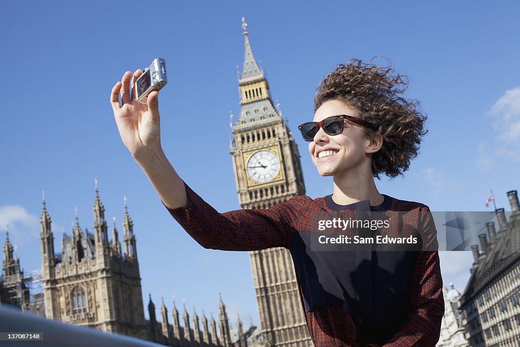 Smiling woman taking self-portrait with digital camera below Big Ben clocktower