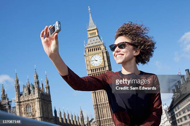 smiling woman taking self-portrait with digital camera below big ben clocktower - foreign stock pictures, royalty-free photos & images
