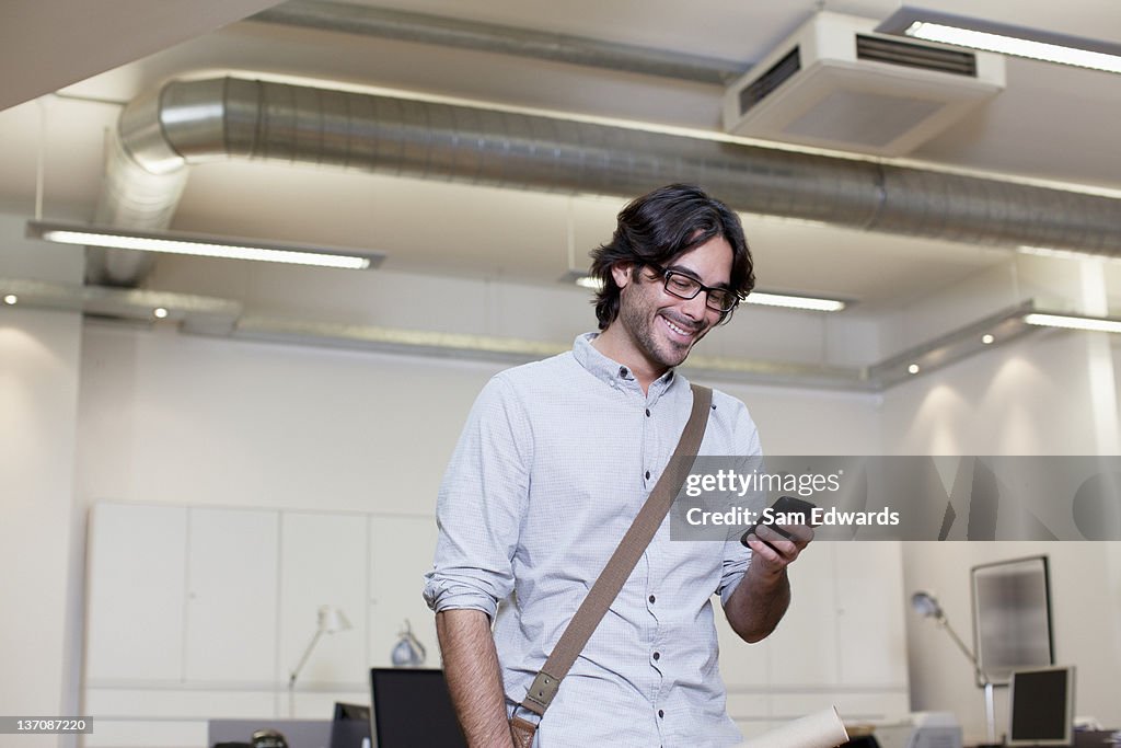 Smiling businessman text messaging on cell phone in office
