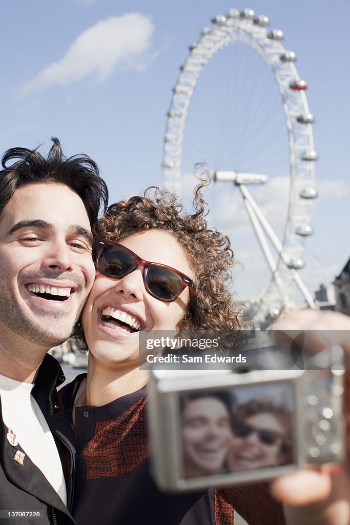 Happy couple taking self-portrait with digital camera in front of ferris wheel