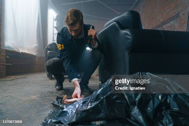 un agente del fbi en la escena del crimen examina un cadáver debajo de una bolsa de plástico negra - killing fotografías e imágenes de stock