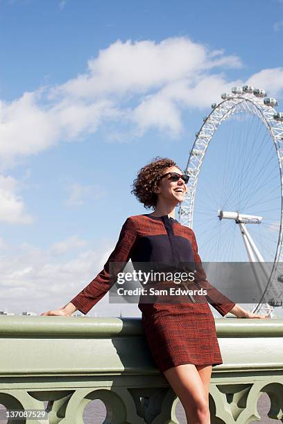 smiling woman leaning on railing of bridge in front of ferris wheel - millennium wheel stock pictures, royalty-free photos & images