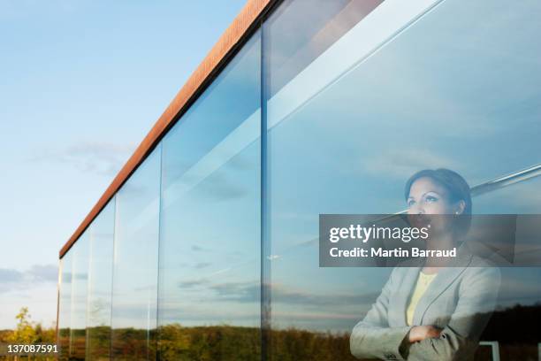 pensive businesswoman with arms crossed in office window - verlangen stockfoto's en -beelden