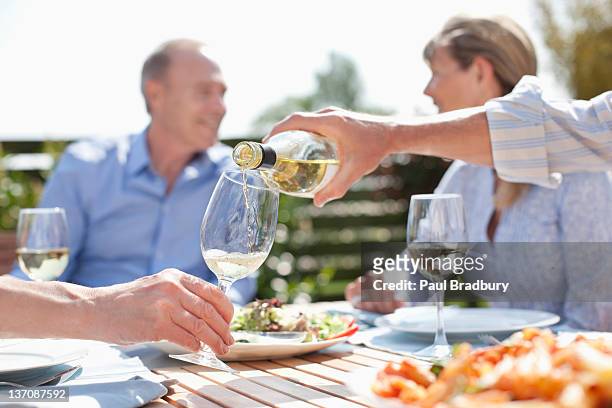 man pouring wine at sunny table - senior women wine stock pictures, royalty-free photos & images