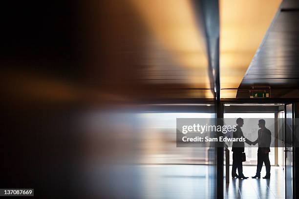 businessman shaking hands together in corridor - business stock pictures, royalty-free photos & images