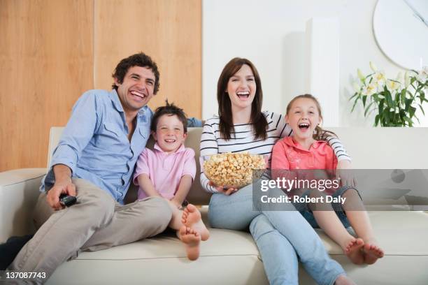 laughing family watching tv on sofa - portrait of family sitting on sofa together stock pictures, royalty-free photos & images