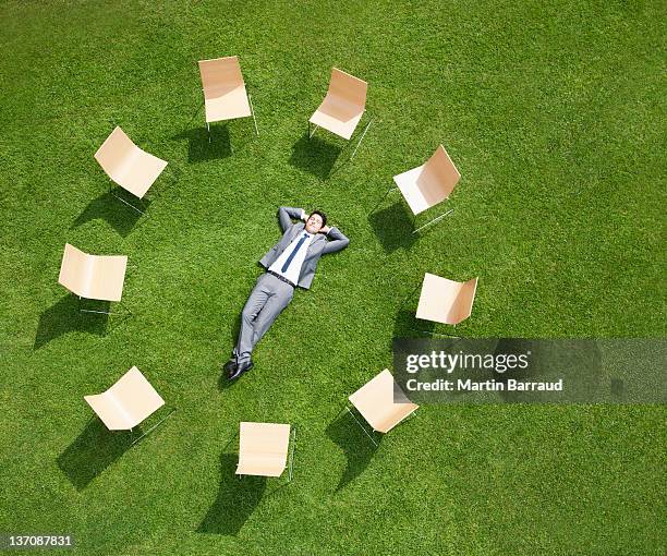 businessman laying in grass surrounded by chairs - hands behind head stock pictures, royalty-free photos & images